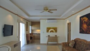 A spacious living area with a ceiling fan, a television, a sofa, and a dining area with a kitchen in the background. - Baan Suan Lalana Tc Floor 5 Room (Pattaya)