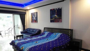 A modern bedroom with a large bed, a sofa, and a small table. There are two paintings on the wall and a sliding glass door leading to an outdoor area. - Baan Suan Lalana Td Floor 2 Room 203 (Pattaya)