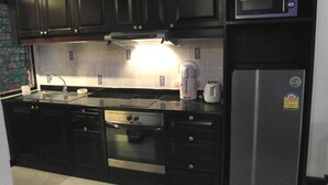 A modern kitchen with dark cabinetry, stainless steel appliances, and a microwave. - Baan Suan Lalana Td Floor 2 Room 203 (Pattaya)