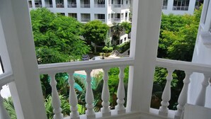 A balcony with white balustrades overlooking a lush green courtyard with trees and a white building in the background. - Baan Suan Lalana Sa Floor 4 Room 415 (Pattaya)