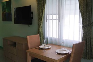 A dining area with a wooden table set for two, a television on the wall, and a window with sheer curtains. - Baan Suan Lalana Sa Floor 4 Room 415 (Pattaya)