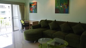 A modern living room with a sectional sofa, a glass coffee table, and two abstract paintings on the wall. - Baan Suan Lalana Sa Floor 4 Room 415 (Pattaya)