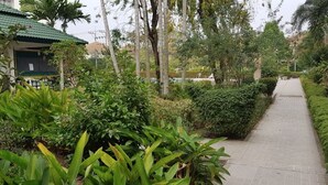 A pathway flanked by lush greenery and a building with a green roof. - Baan Suan Lalana Sa Floor 4 Room 415 (Pattaya)