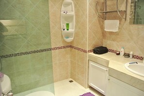 A bathroom with a shower, a sink, and a toilet. There is a towel rack and a soap dispenser on the wall.