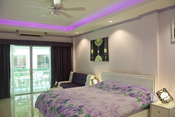 A bedroom with a bed, a ceiling fan, a nightstand, a decorative wall piece, and a view of a balcony with outdoor furniture.