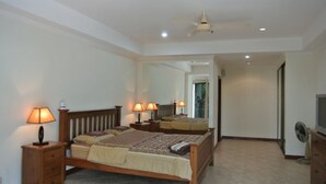 Une chambre à coucher comprenant un lit, deux tables de chevet avec des lampes, un ventilateur de plafond, un miroir et une commode.