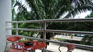Un balcon avec une table en verre et deux chaises rouges, entouré d’une rambarde en métal blanc.