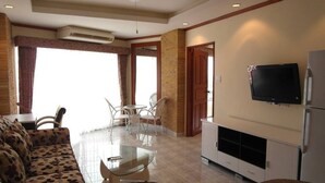 A living room with a sofa, a glass coffee table, a TV, and a kitchen area with a refrigerator. - View Talay 1B Floor 6 Room (Pattaya)