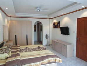 A bedroom with a large bed, a wardrobe, a TV mounted on the wall, and a door.
