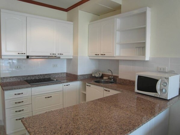 A kitchen with white cabinets, a granite countertop, a microwave, and a sink.