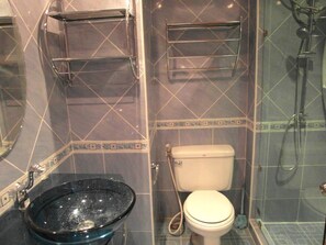 A bathroom with a glass sink, a toilet, and a shower area.