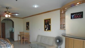 A living room with a sofa, a glass coffee table, a fan, a wooden cabinet, and a 'BAR' sign. - View Talay 8 Floor 25 Room 977 (Pattaya)