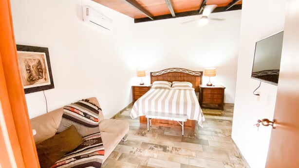 Un dormitorio con cama, lámparas de noche, televisor, techo de madera y sofá estampado.