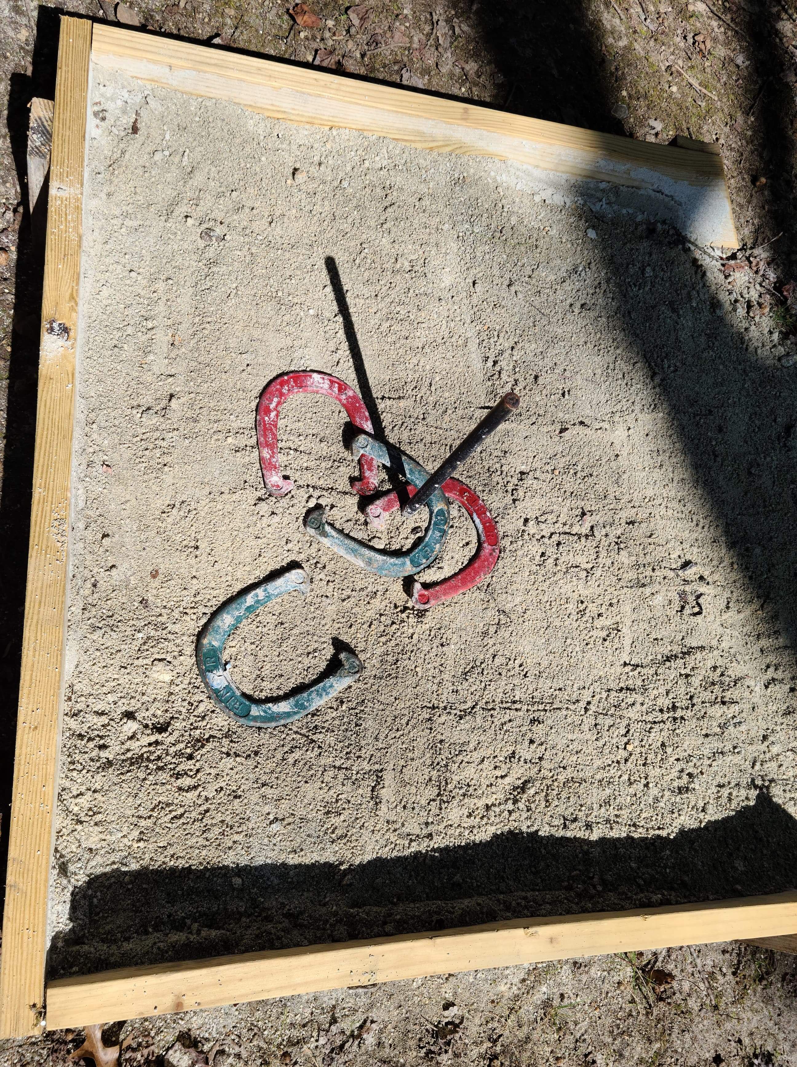 A wooden frame with a metal object inside, possibly a tool or part of a mechanism, on a sandy surface.
