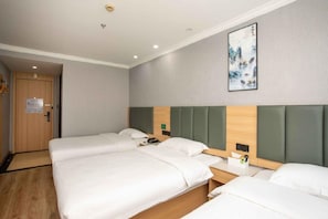 A hotel room with three beds, a wooden door, a framed artwork on the wall, and a small table with a phone and a book.
