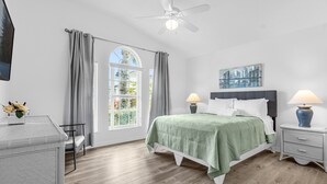 Ein Schlafzimmer mit einem Bett, Nachttischen, einem Deckenventilator und einem Fenster mit Vorhängen.