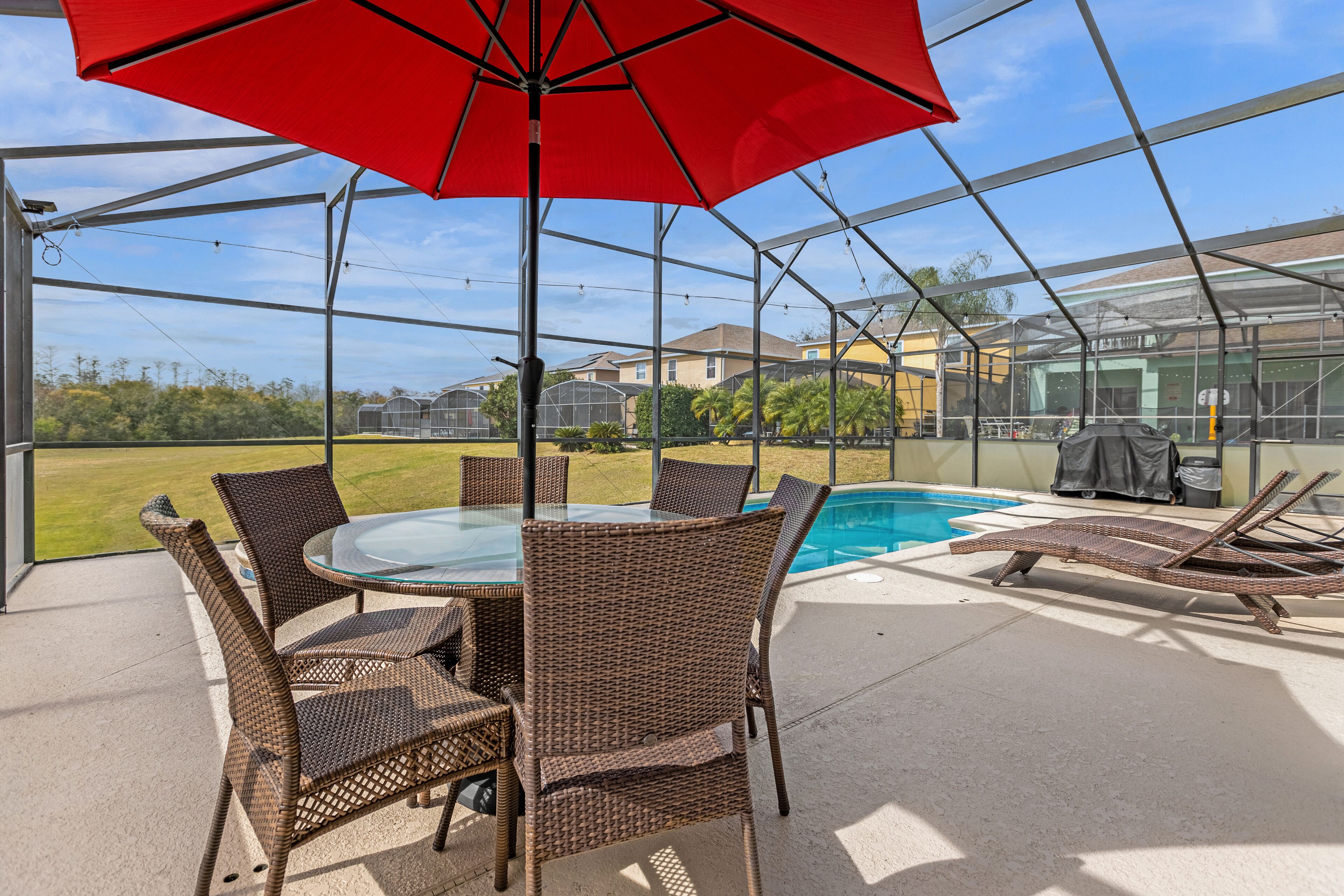 A covered patio area with a glass table and chairs, a red umbrella, and a pool.