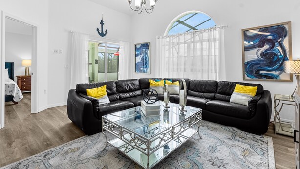 Ein geräumiges Wohnzimmer mit einem schwarzen Leder-Modulsofa, einem Glastisch und einem großen abstrakten Gemälde.