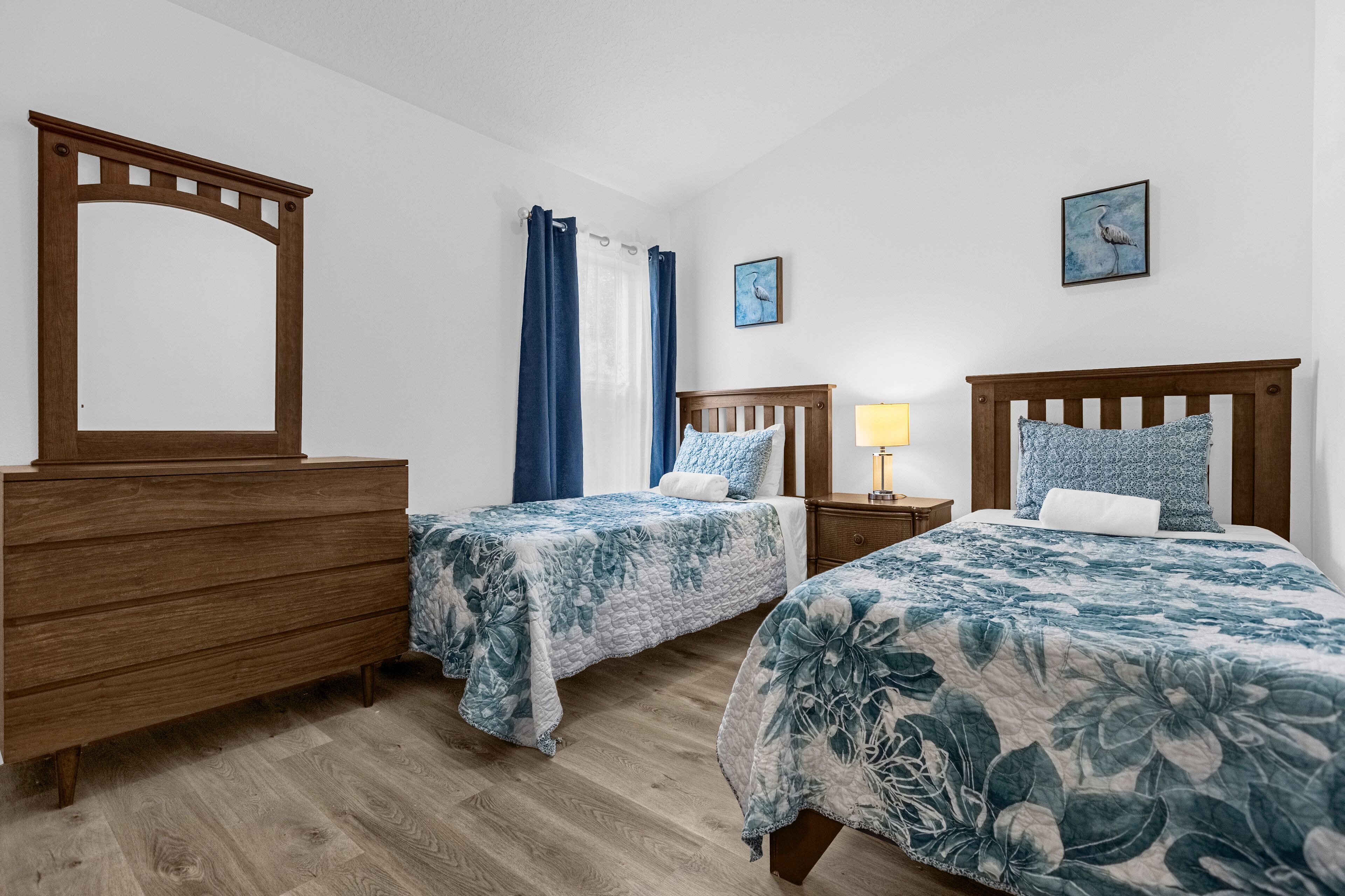 Une chambre avec deux lits, une commode en bois, une table de chevet avec une lampe et un miroir.