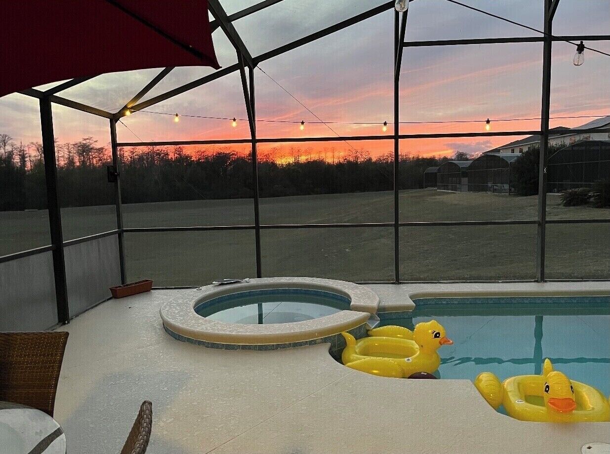 An outdoor swimming pool with inflatable ducks, a covered seating area, and a view of the sunset.