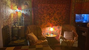 A cozy living room with two armchairs, a small round table, a television, and a large tapestry. - An Indiana Jones Inspired Spectacular Adventure Movie Suite! (Chickamaga)