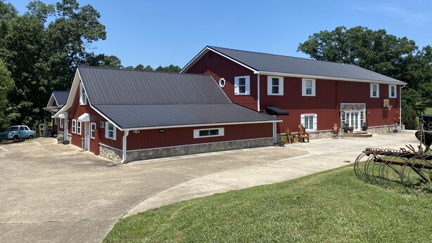 A two-story red building with a metal roof, a stone foundation, and a driveway leading to a parked blue truck. - An Indiana Jones Inspired Spectacular Adventure Movie Suite! (Chickamaga)