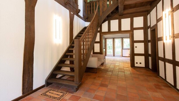 Una escalera de madera con una puerta blanca al final que da a una habitación con piso de baldosas y vistas al exterior.