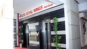 The entrance to Hotel Royal Wings, 4th Floor, with a red carpet, black and white striped exterior, and two potted plants.