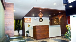 A hotel reception area with a wooden reception desk, a clock, and a wall-mounted fan.
