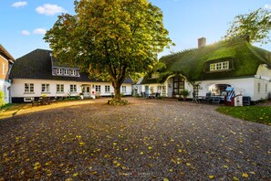 Ein Innenhof mit Kiesweg, einem großen Baum und traditionellen Gebäuden mit Strohdächern.