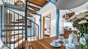 A modern interior with a wooden dining table set for tea, a staircase with a metal railing, and a view into a bedroom.