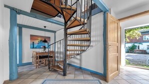 A spiral staircase with wooden steps and metal railings, leading to a room with a dining area and a view of the outside.
