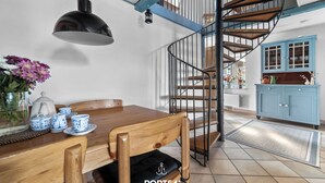 A dining area with a wooden table, chairs, a black pendant light, and a blue cabinet in the background.