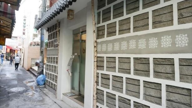 A narrow street with traditional architecture, including a building with a tiled roof and a decorative wall. - Oh My Inn (Seoul)