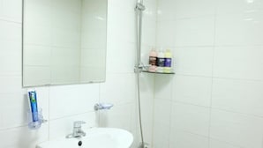 A bathroom with a white sink, a mirror, and a shower. There are toiletries on a shelf. - Oh My Inn (Seoul)