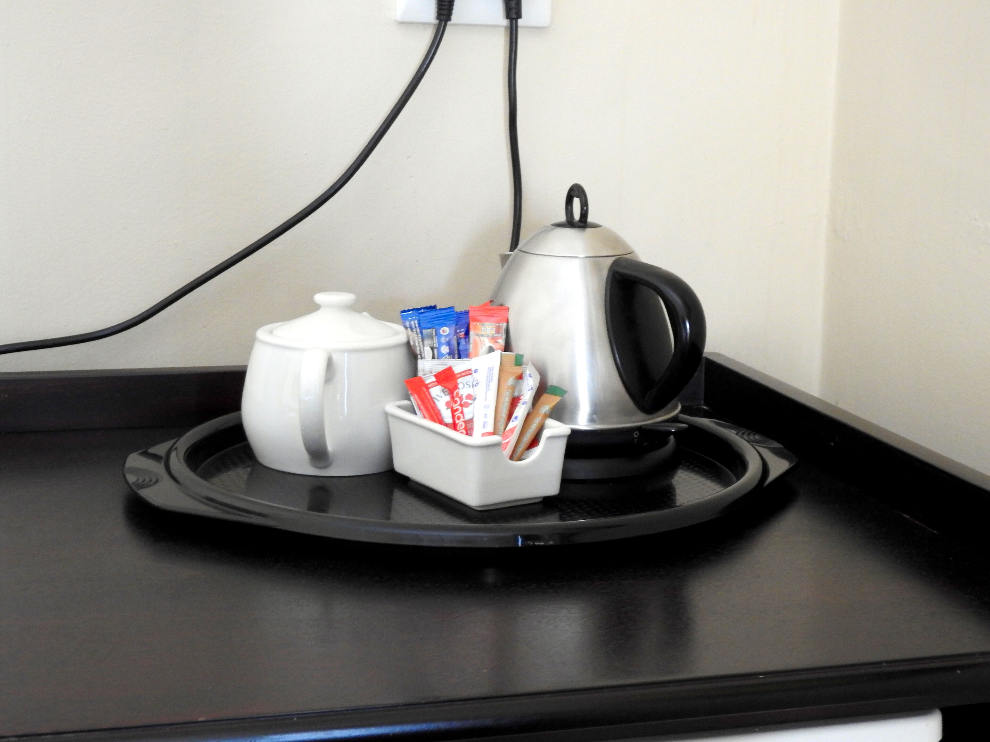 A kitchen counter with a kettle, a coffee pot, and a container holding coffee packets.