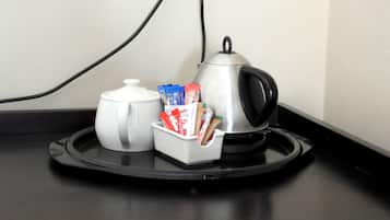 A kitchen counter with a kettle, a coffee pot, and a container holding coffee packets.