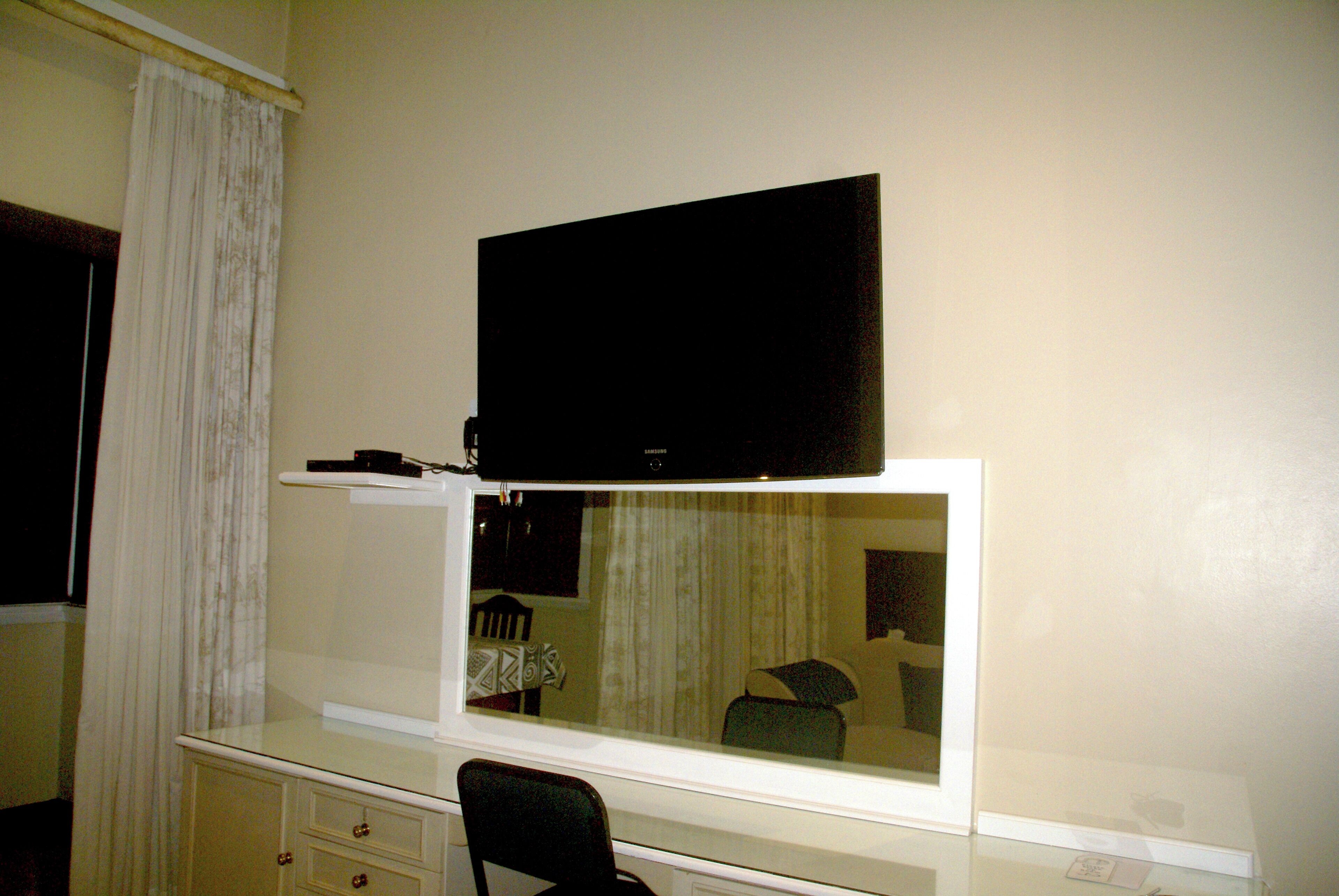 A room with a TV mounted on a white cabinet, a chair, and a table with a chair.