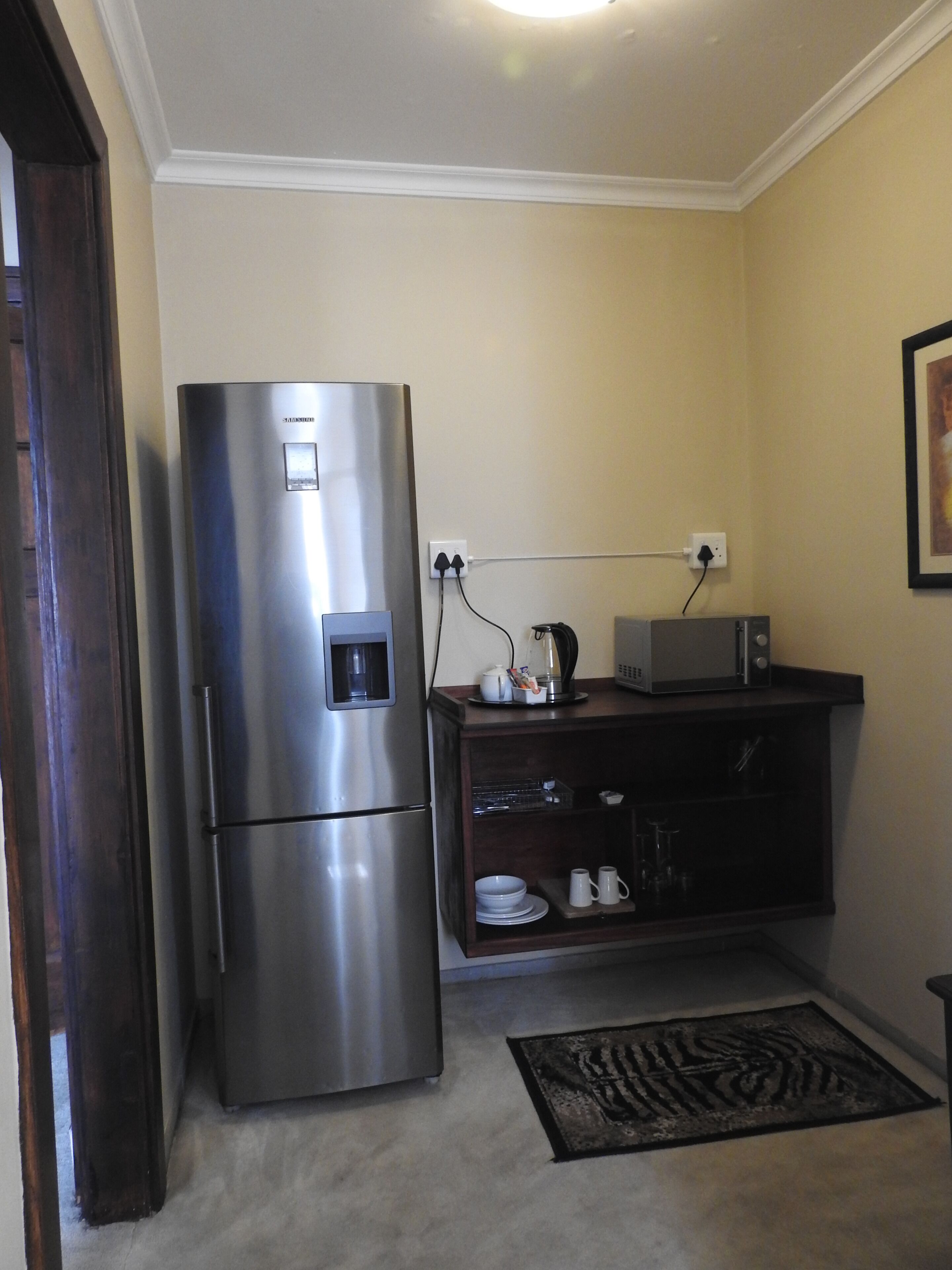 A compact kitchen with a stainless steel refrigerator, a microwave, and a dark wooden cabinet below.