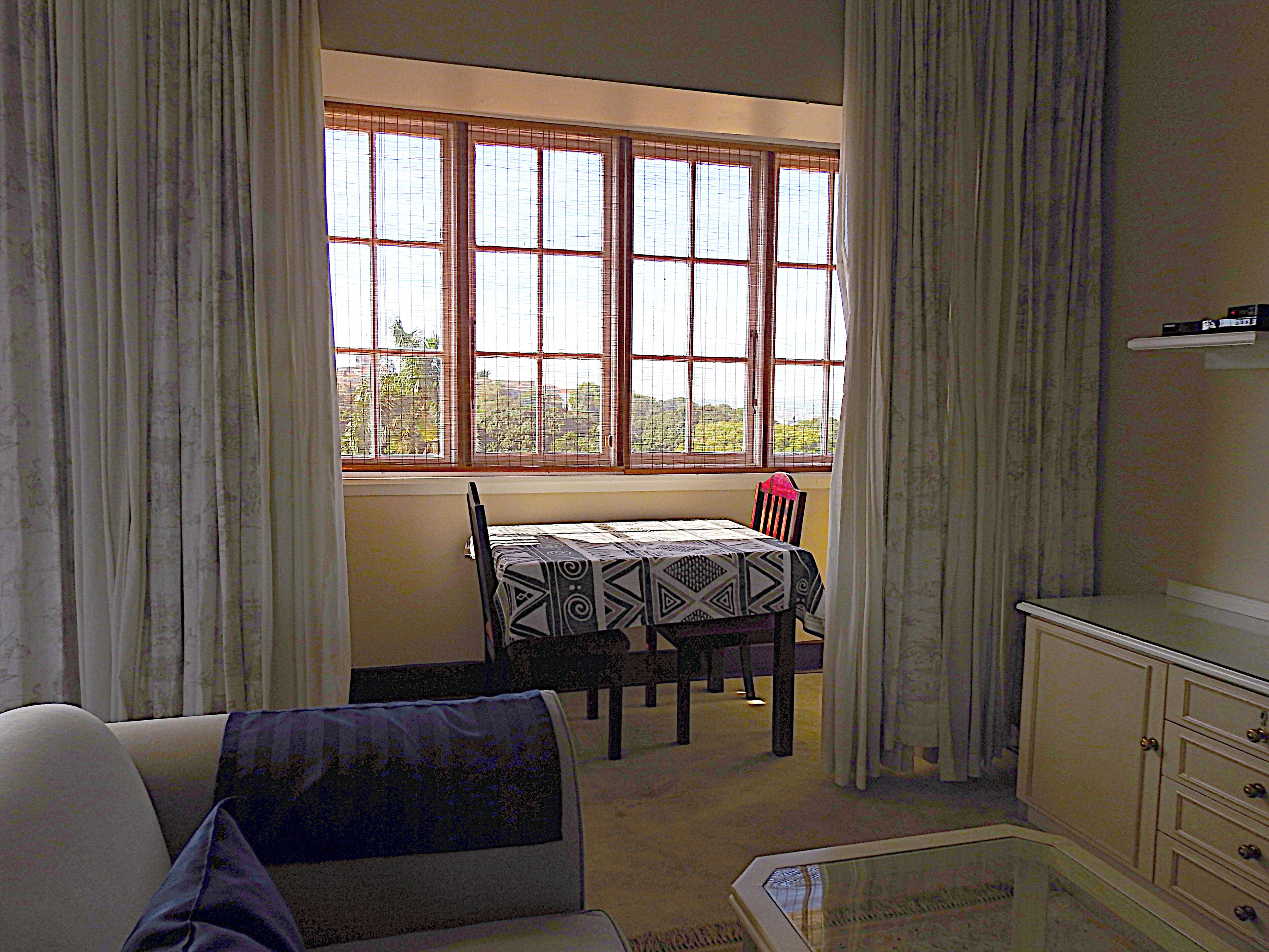 A room with a dining table set for two, a sofa, and a cabinet.