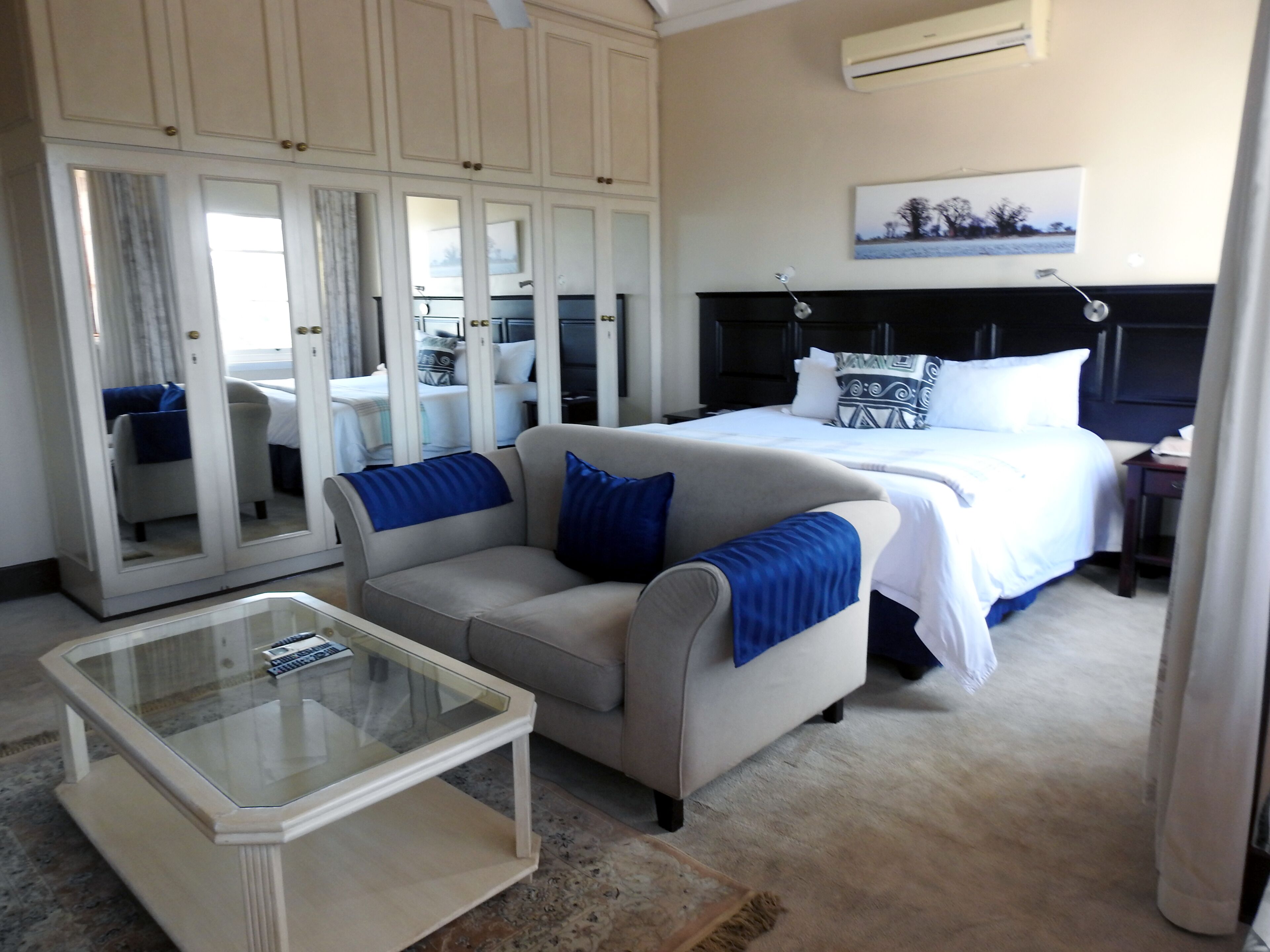 Habitación de hotel con cama, sofá, una mesita de centro de vidrio y un armario con espejos.