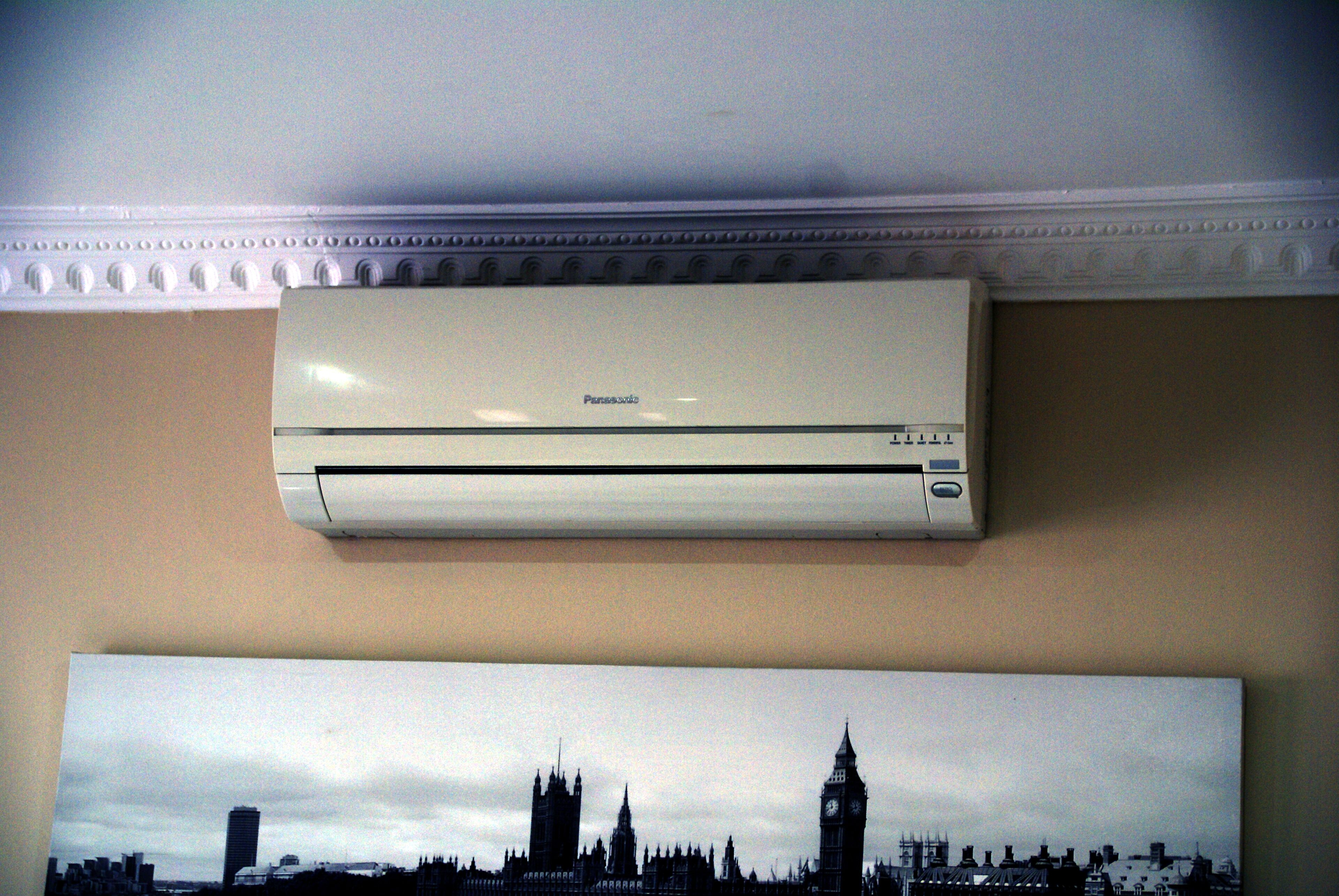 A white Panasonic air conditioner mounted on a wall above a framed picture of a city skyline.