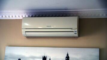 A white Panasonic air conditioner mounted on a wall above a framed picture of a city skyline.