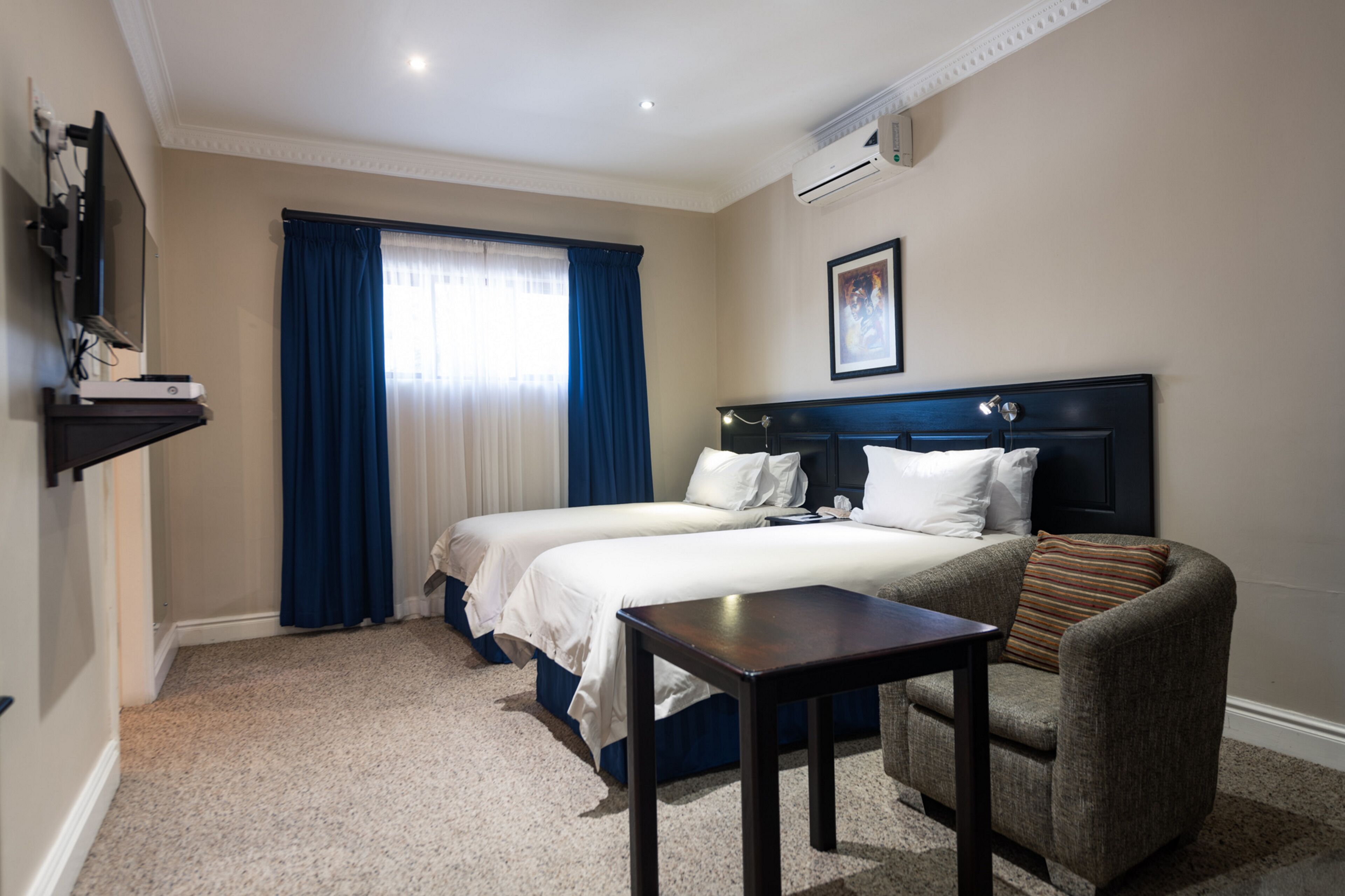 Hotellihuone, jossa on kaksi sänkyä, työpöytä, tuoli, televisio ja ilmastointilaite.