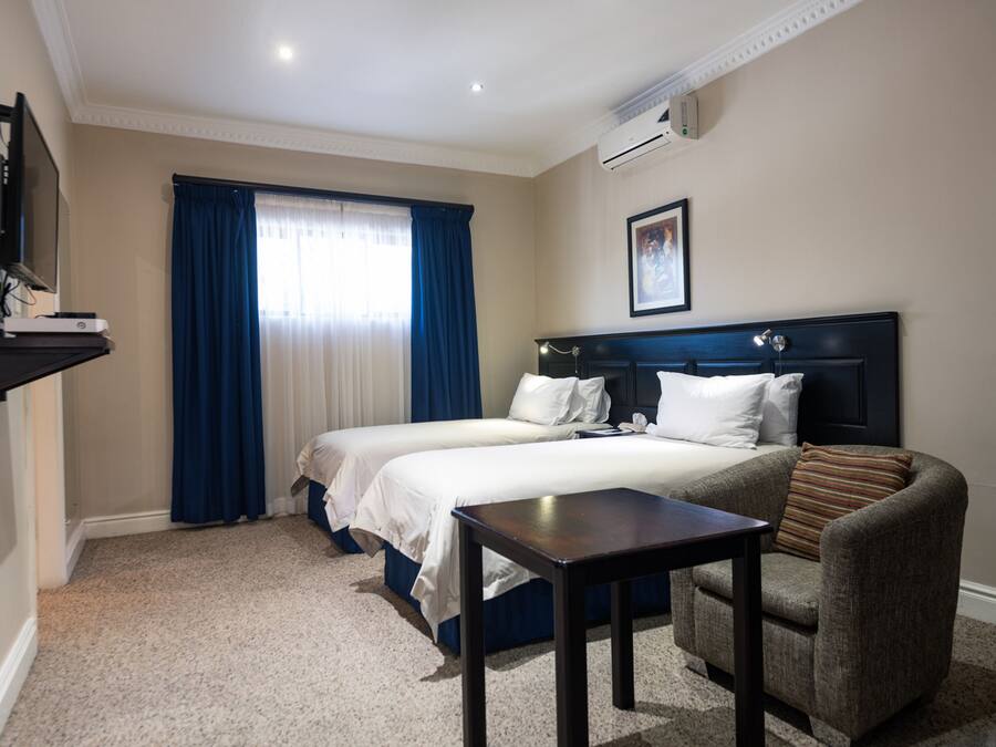 Hotellihuone, jossa on kaksi sänkyä, työpöytä, tuoli, televisio ja ilmastointilaite.