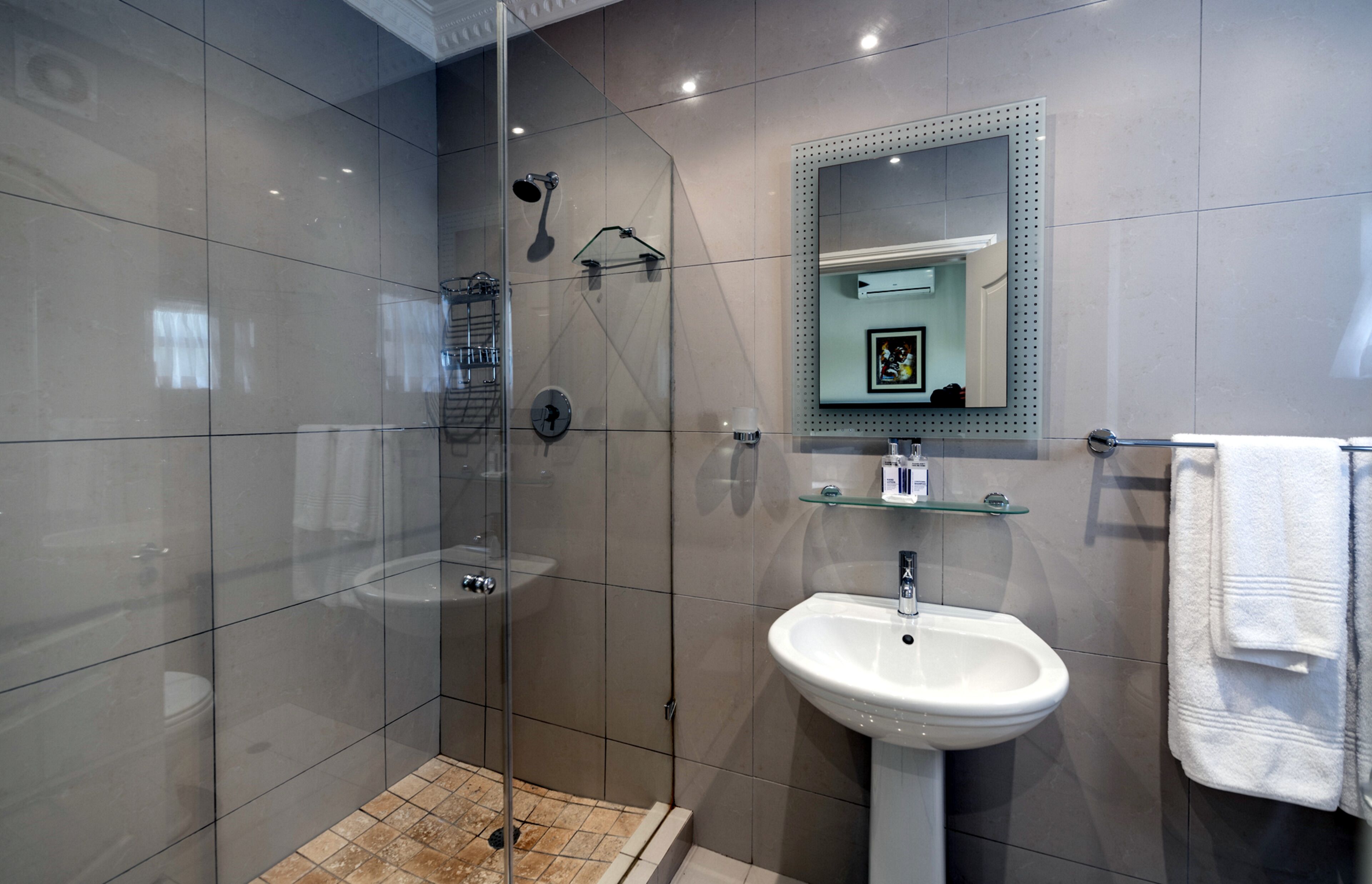 Un baño moderno con ducha de vidrio, lavamanos pedestal y espejo con marco decorativo.