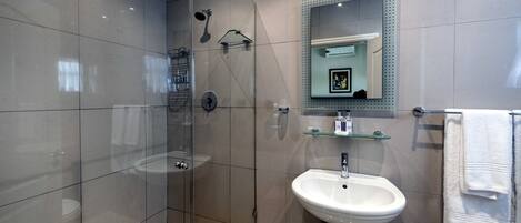 Un baño moderno con ducha de vidrio, lavamanos pedestal y espejo con marco decorativo.