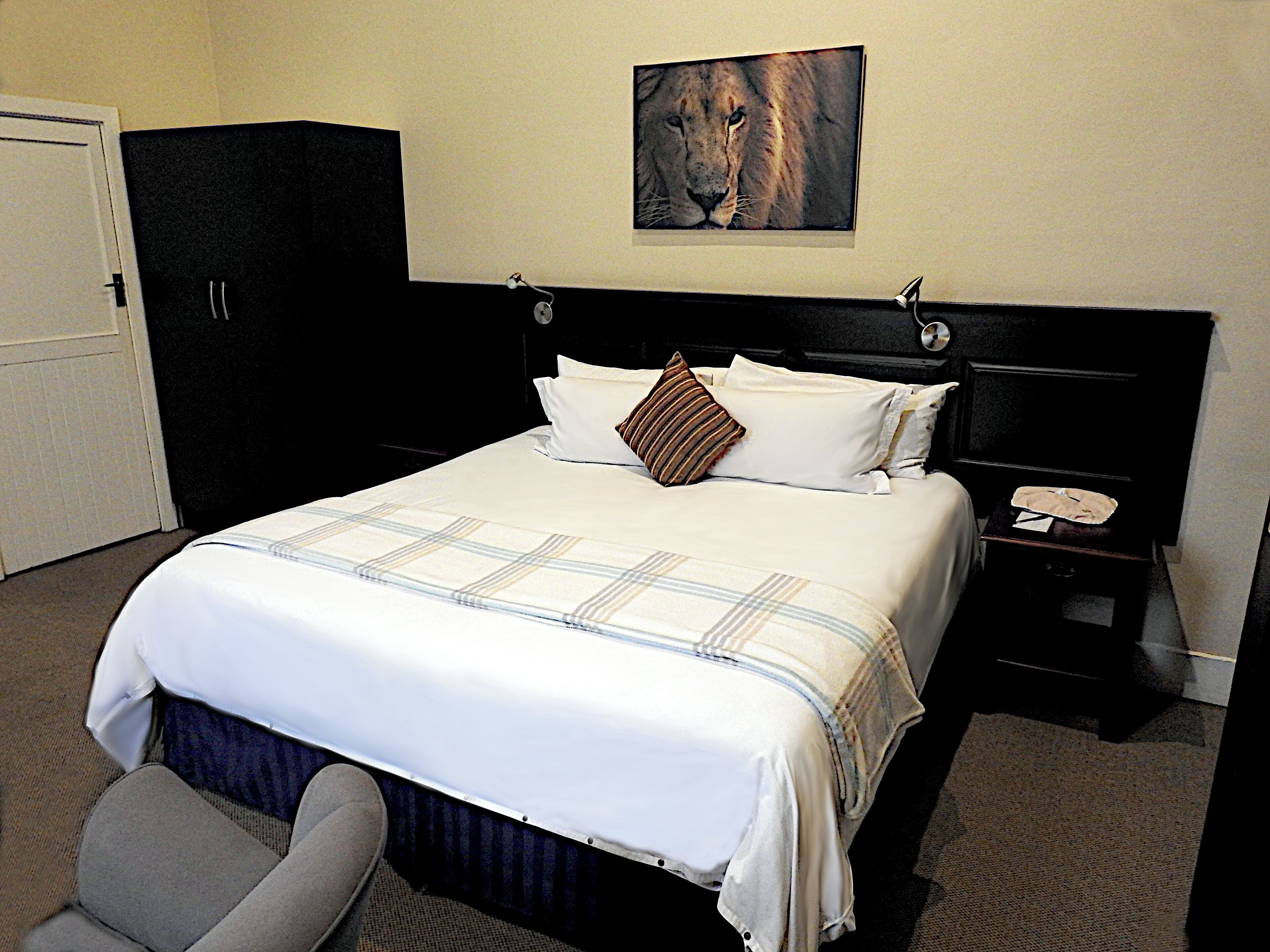 A hotel room with a large bed, a headboard, a nightstand, a telephone, and a painting of a lion on the wall.