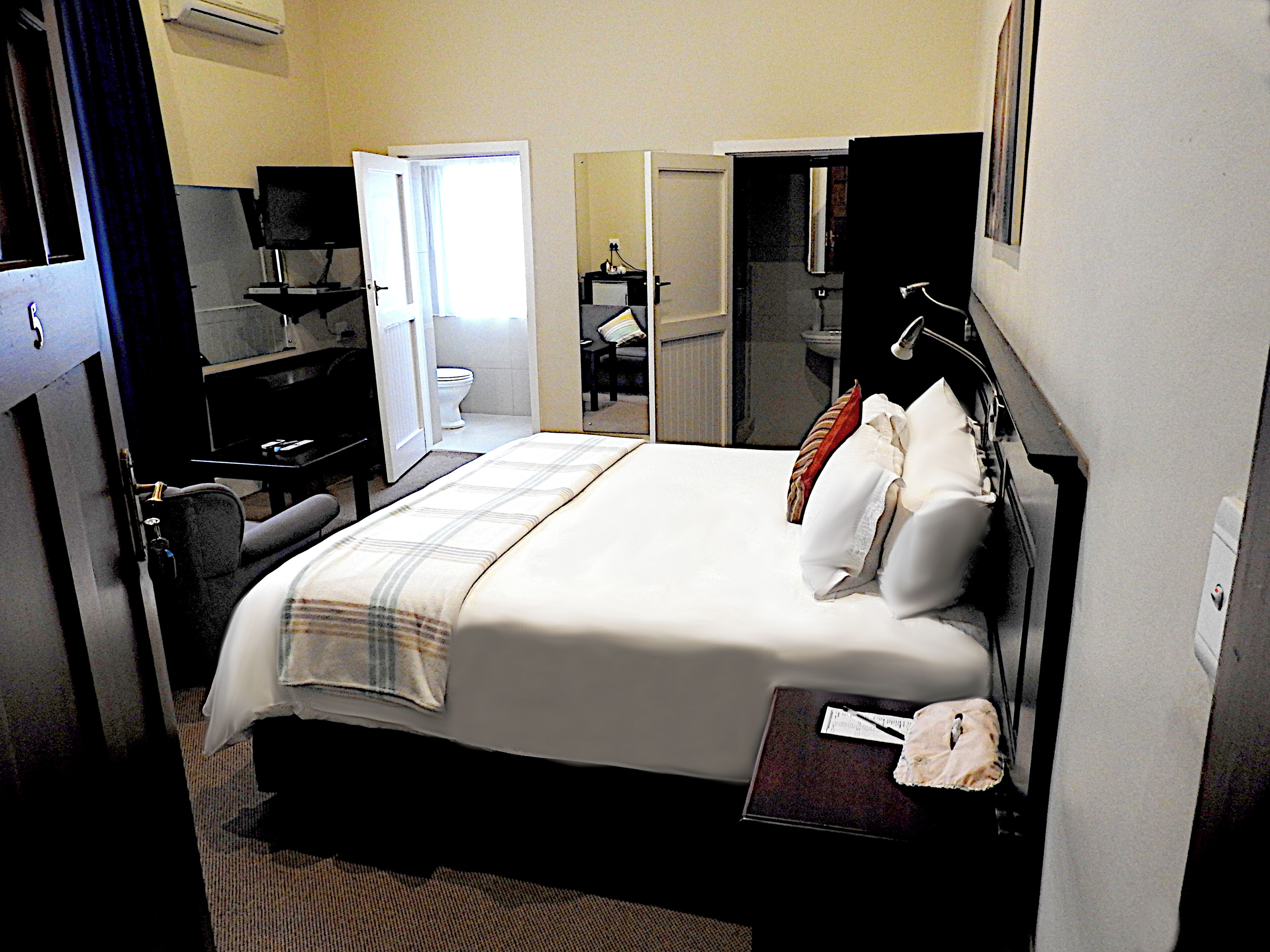 Habitación de hotel con cama, escritorio, silla, televisor y baño visible a través de una puerta abierta.