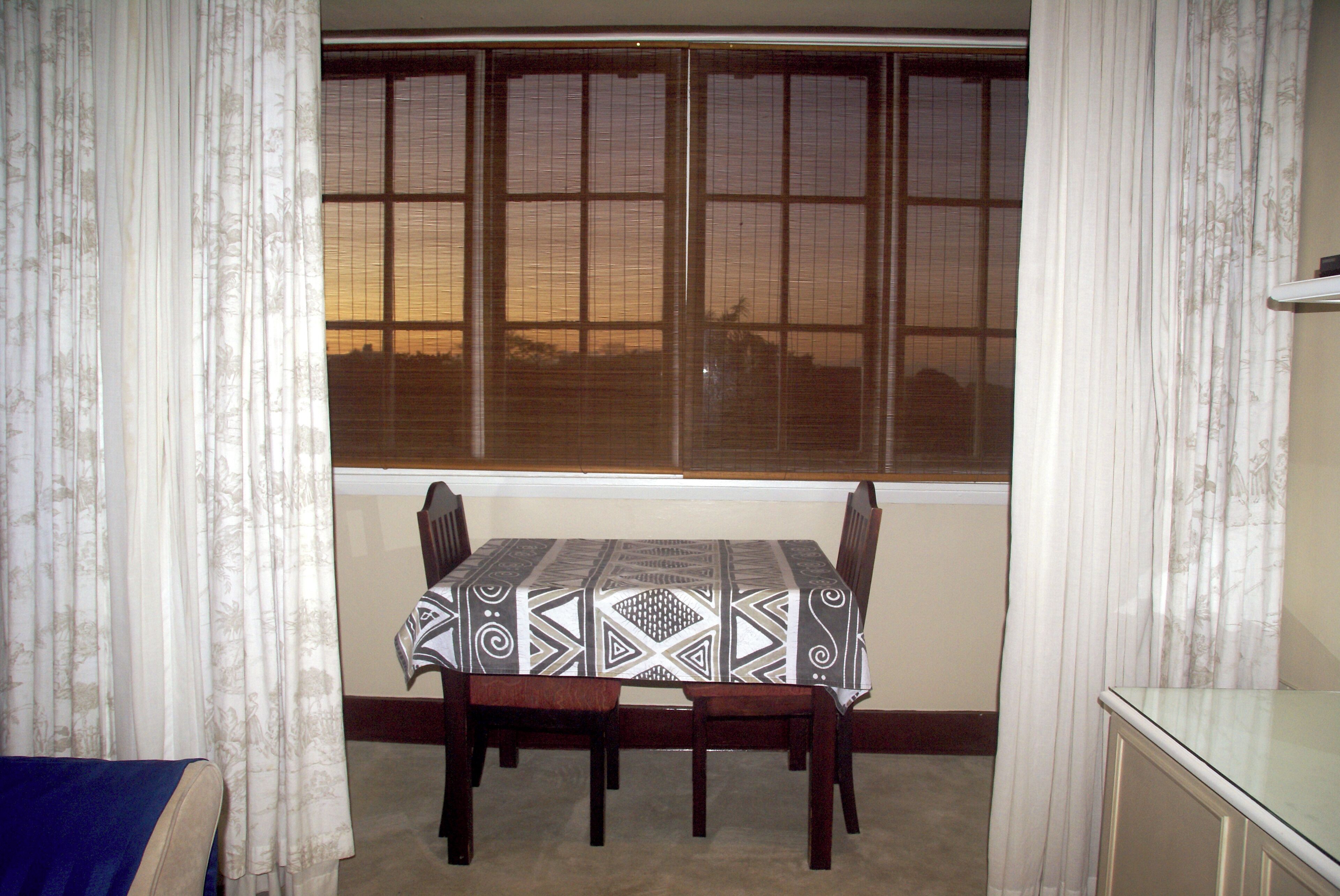 A dining area with a table set for four, a window with blinds, and a blue sofa.